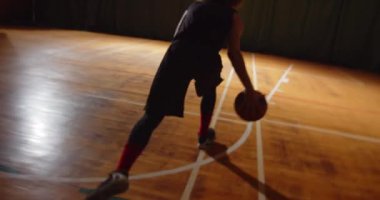 Genç kıvırcık profesyonel basketbolcu basket topunu potaya fırlatıyor. Gece karanlığının silueti arka pencereden süzülüyor.