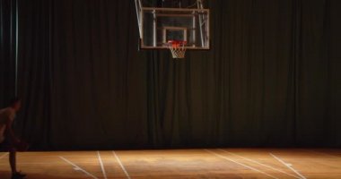 Beyaz tenli genç basketbolcu topu potaya atıyor. Kazanan gece spor salonu parkesi sallanıyor.