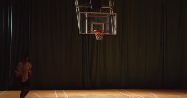 Młody biały koszykarz rzuca piłkę do kosza. Zwycięzca wieczorny parkiet hali sportowej — Wideo stockowe