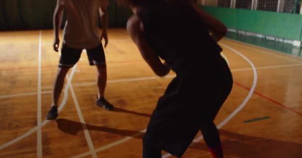 Dos jóvenes jugadores de baloncesto juegan basket ball competición aficionados sala deportes parquet driblar ataque noche juego — Vídeo de stock