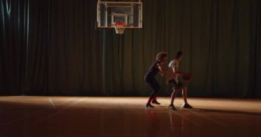 Toplamda iki genç basketbolcu basketbol oynuyor amatörler salon spor parketi siluetleri rakip savunma bloğu gece maçında top sürüyor.