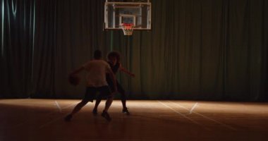 İki genç basketbolcu basketbol oynuyor. Uzak mesafe savunma oyunu. Gece yarısı karanlık siluetleri ışık huzmesi.