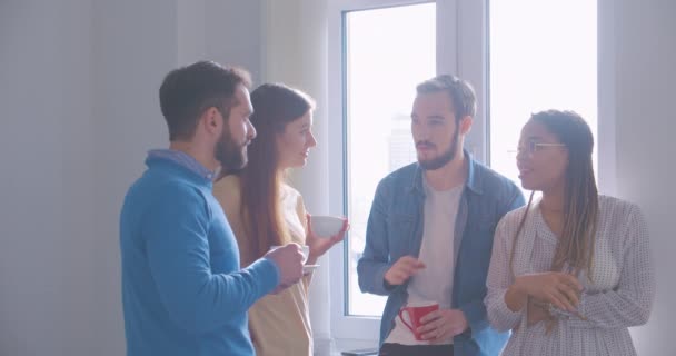 Czterech różnych wielorasowych kolegów w biurze przerwa na kawę rozmowa smartfon dyskusja — Wideo stockowe