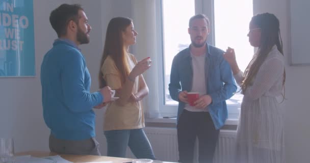 Čtyři rozmanité multiraciální kolegové v kanceláři přestávka na kávu konverzace konverzace diskuse slunný pokoj odpočinek relaxace smích — Stock video