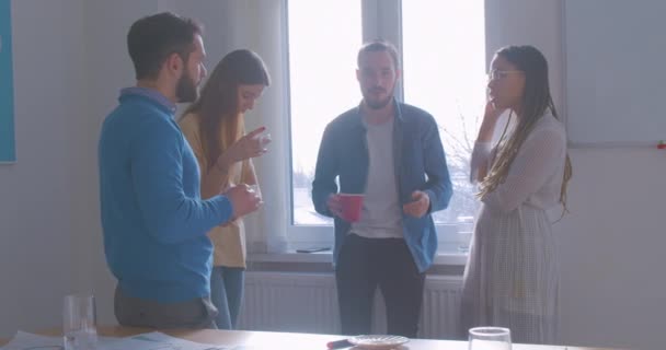 Four diverse multiracial colleagues in the office coffee break conversation discussion sunny room rest joke laughter — Stock Video