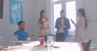 Ofisteki dört farklı ırktan iş arkadaşı kahve molasında akıllı telefon ve modern internet problemi kullanıyor.