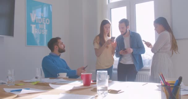 Cuatro diversos colegas multirraciales en el café de la oficina usan teléfono inteligente moderno internet problema risa vídeo broma — Vídeo de stock