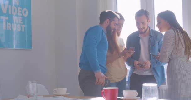 Four diverse multi-racial colleagues at office coffee break use smartphone internet laughing video joke — Stock Video