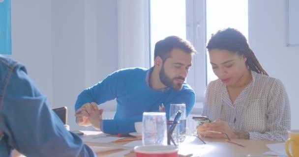 Jóvenes colegas en una oficina soleada usan teléfonos inteligentes muestran fotos divertidas se comunican — Vídeos de Stock