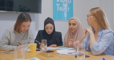 Kendine güvenen dört farklı kadın meslektaşı genç ofis çizelgeleri iş fikri planlıyorlar.