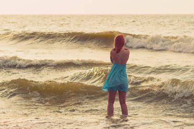 Deniz arka planında pembe saçlı bir kadın poz veriyor.