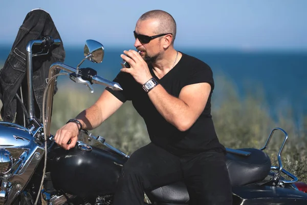hot biker is smoking sitting on the motorcycle. Brutal man in glasses against the bike