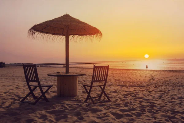 Деревянный стол и стулья с зонтиком на пляже — стоковое фото