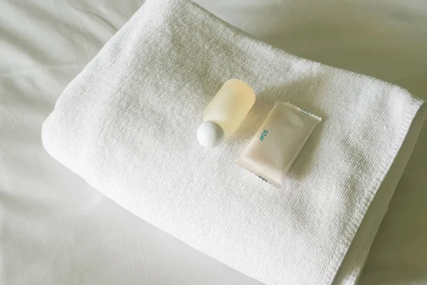 Goedkoop Hotel Bed met Shampoo en zeep fles ingesteld op witte handdoek. — Stockfoto