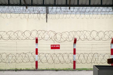 Keskin dikenli tel ve yüksek beton duvar ile koruma çit.