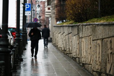 Şehirde yağmur yağıyor. Yağmur sırasında şemsiye altındaki insanlar ıslak sokaklarda gezerler..