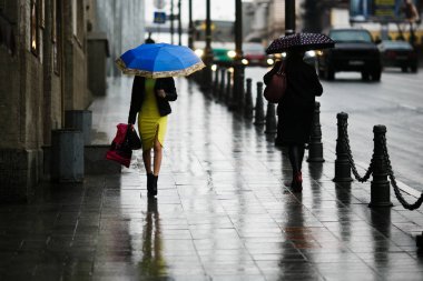 Şehirde yağmur yağıyor. Yağmur sırasında şemsiye altındaki insanlar ıslak sokaklarda gezerler..