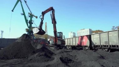 Yaz, 2019 - Nakhodka, Primorsky Bölgesi - Genel plan. Büyük bir kova taşıyan bir vinç demiryolu vagonlarına kömür yüklüyor. Nakhodka limanında vagonlara kömür dolduruluyor..