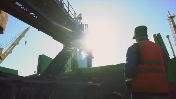 作業服を着た男が貨物船を背景に桟橋に立っており コンベアを使用して石炭を積み込むプロセスを制御しています 海上貨物船への石炭積込み — ストック動画