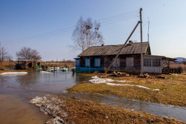 Rus köyü. Baharda alçak ahşap çitlerin arkasında eski bir köy ahşap evi. Rusya 'da bir köy kulübesinin arka planında bahar birikintileri.