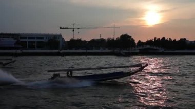 Ağır çekimde çekim. Chao Phrai Nehri, Bangkok 'ta. Turist uzun botu batan güneşe karşı nehirde yüzer..