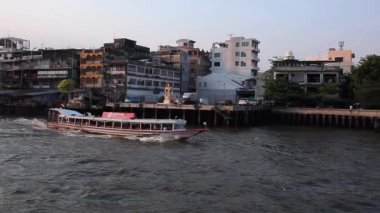 Nisan 2019 - Tayland, Bangkok - Chao Phraya Nehri, Bangkok. Sloumotion Tayland 'ın ana nehri boyunca yüzen bir turist teknesi Bangkok' un arka planında ve gecekondu mahallelerinde yüzüyor..