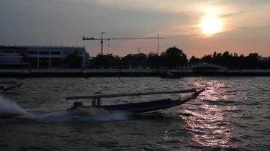 Ağır çekimde çekim. Chao Phrai Nehri, Bangkok 'ta. Turist uzun botu batan güneşe karşı nehirde yüzer..