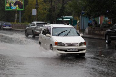 2015 yazında - Vladivostok, Rusya - Vladivostok sokakları yağmurdan ıslandı. Yağmur sırasında, su birikintileri arasında arabalar şehrin merkezinden geçer..