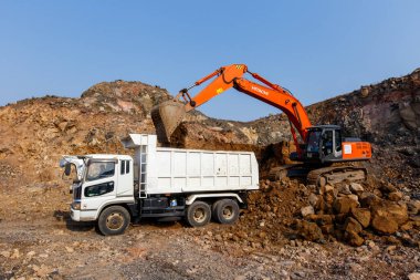 2015 sonbaharında - Primorsky Krai, Rusya - Endüstriyel fotoğrafçılık. Taş ocağındaki kazıcılar doğal taş ve toprak çıkarırlar. Ağır kova vagonlar kamyonlara toprak yüklüyor.