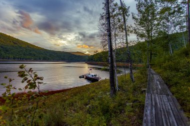 Güzel manzara. Zeya rezervuarı, Amur bölgesi. Güzel bir günbatımının arkaplanına karşı kıyıya demirlemiş küçük bir tekne. Sudaki günbatımının yansıması..