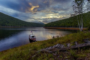 Güzel manzara. Zeya rezervuarı, Amur bölgesi. Güzel bir günbatımının arkaplanına karşı kıyıya demirlemiş küçük bir tekne. Sudaki günbatımının yansıması..