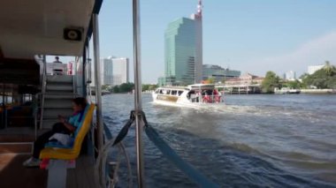 2019 baharında, Bangkok, Tayland 'da Yavaş Hareket. Zevk teknesinin yanından Bangkok 'taki Chao Phraya Nehri' ne bakın. Bangkok 'un ana nehri boyunca uzanan turistik tekne, yüksek binaların arka planına karşı.