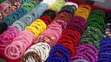 Yakın plan. Birçok renkli boncuk bileziği gece pazarında tezgahın üzerinde. Elde bilezik satışı.