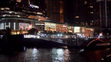 2019 yazında Bangkok, Tayland 'da Bangkok' un ana nehri Chhao Praia boyunca bir turist teknesinde gece yürüyüşü. Turistlerle dolu bir tekne yüksek binaların ve parlak alışveriş merkezlerinin önünden yüzüyor..