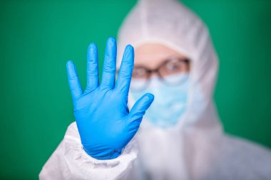 COVID-19. 2019 Novel Coronavirus (2019-nCoV) konsepti. Beyaz veba önlüklü ve mavi lastik eldivenli genç kız doktor yeşil arka planda izole edilmiş stop hareketi gösteriyor.