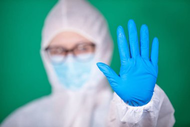 COVID-19. 2019 Novel Coronavirus (2019-nCoV) konsepti. Beyaz veba önlüklü ve mavi lastik eldivenli genç kız doktor yeşil arka planda izole edilmiş stop hareketi gösteriyor.