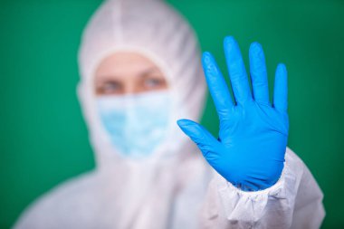 COVID-19. 2019 Novel Coronavirus (2019-nCoV) konsepti. Beyaz veba önlüklü ve mavi lastik eldivenli genç kız doktor yeşil arka planda izole edilmiş stop hareketi gösteriyor.