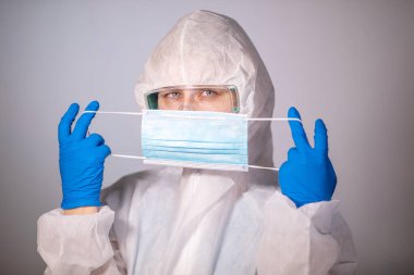 COVID-19. 2019 Novel Coronavirus (2019-nCoV) konsepti. Beyaz koruyucu veba önlüklü genç bir doktor yüzüne tıbbi bir maske takıp kameraya bakıyor.