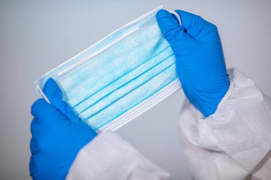 COVID-19. Yığının üzerinde yüz maskeleri var. Salgın geçmişi. Yakın plan. Koruyucu veba önleme giysisi giymiş bir tıp çalışanı plastik tek kullanımlık eldivenli bir maske tutuyor.