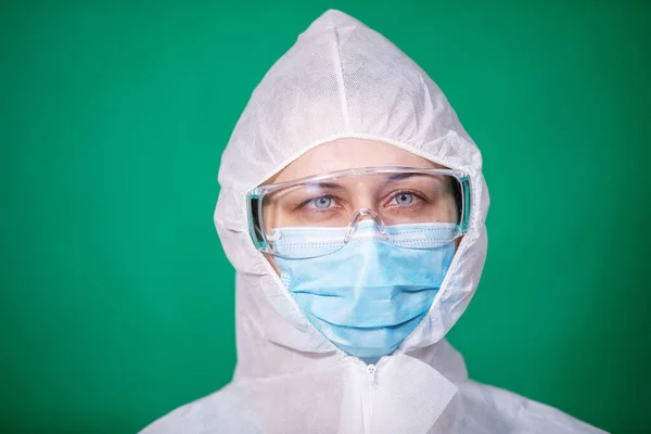 COVID-19. 2019 Novel Coronavirus (2019-nCoV) concept. face close-up portrait of a young female doctor in a protective white anti-plague suit on a medical face mask. on a blue background.