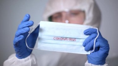COVID-19. 2019 Novel Coronavirus (2019-nCoV) konsepti. Beyaz koruyucu veba önlüklü genç bir doktor elinde Coronavirus yazısıyla tıbbi bir maske tutuyor.