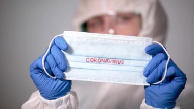 COVID-19. 2019 Novel Coronavirus (2019-nCoV) konsepti. Genç doktor yüzüne koruyucu beyaz sisli bir paltoyla Coronavirus yazısıyla maske takıyor.
