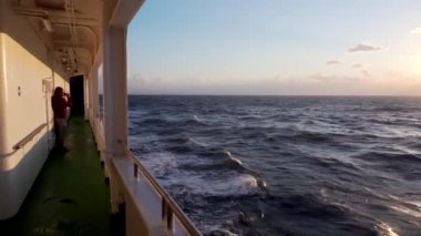 2019 Baharı - Vladivostok, Rusya - Doğu Rüya Yolcu Feribotu. Yolcu, yolcu feribotunun yürüyen güvertesinden gün batımına ve deniz dalgalarına hayran. Denizde güzel bir gün batımı.