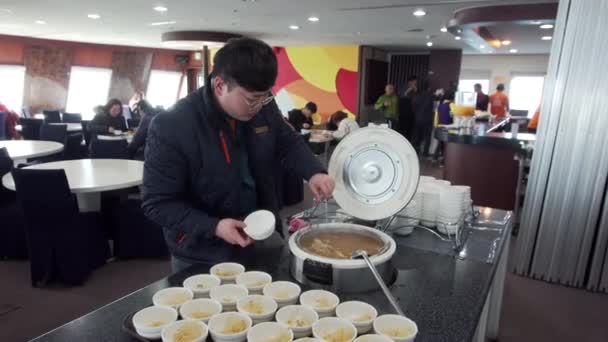 2019年春 日本海 ロシア Eastern Dream旅客フェリークルーズ中 若い男の料理人は フェリーのダイニングルームでスウェーデンの朝食中に皿の上にみそ汁を置きます — ストック動画