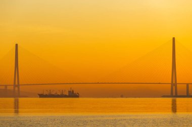 Deniz kenti Vladivostok 'ta şafak vakti. Vladivostok 'taki Russky Adası' na uzanan Vostochny Boğazı 'ndaki Rus köprüsünde, sakin deniz sırasında, altın bir şafağın arka planına karşı kablo destekli Rus köprüsü..