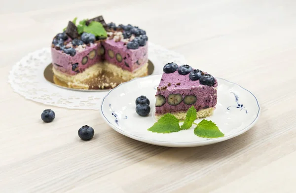 The piece of raw vegan blueberry cake on the light wooden surfac — Stock Photo, Image