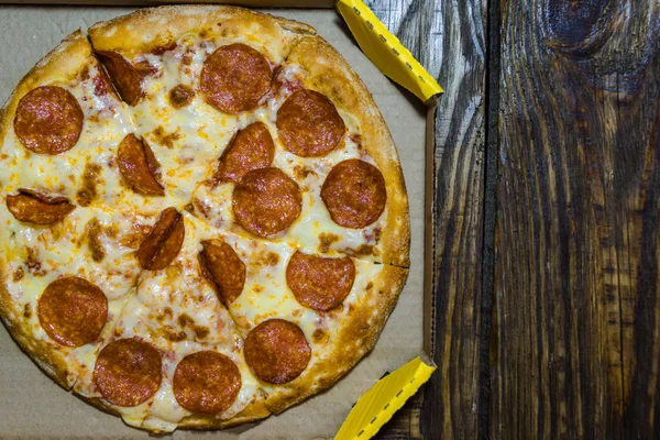 Pizza italiana en caja de cartón sobre la mesa de madera. Un fondo texturizado. Copiar lugar de pasta . — Foto de Stock