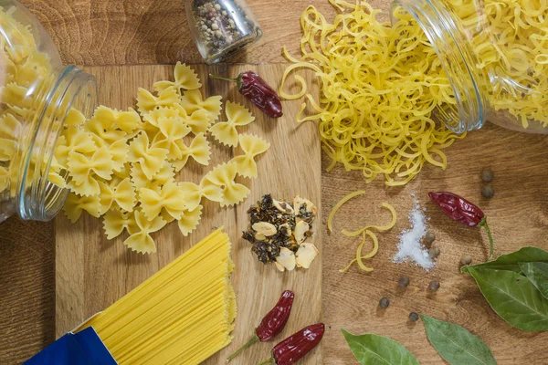 On a wooden table pasta of different types and spices for cooking pasta. Simple village food.