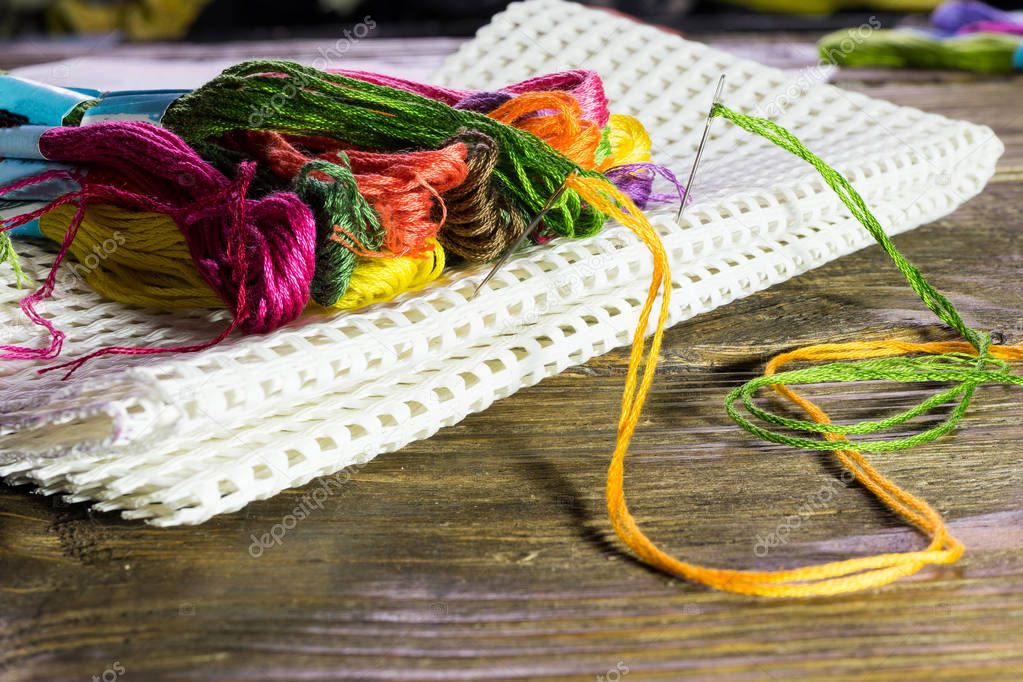 floss of different colors lying on a large canvas stuck it with needles. Wooden rustic table