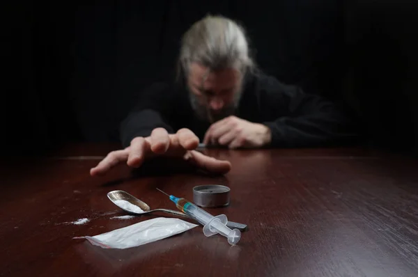 Narkoman u stolu táhne ruku do stříkačky s dávkou — Stock fotografie